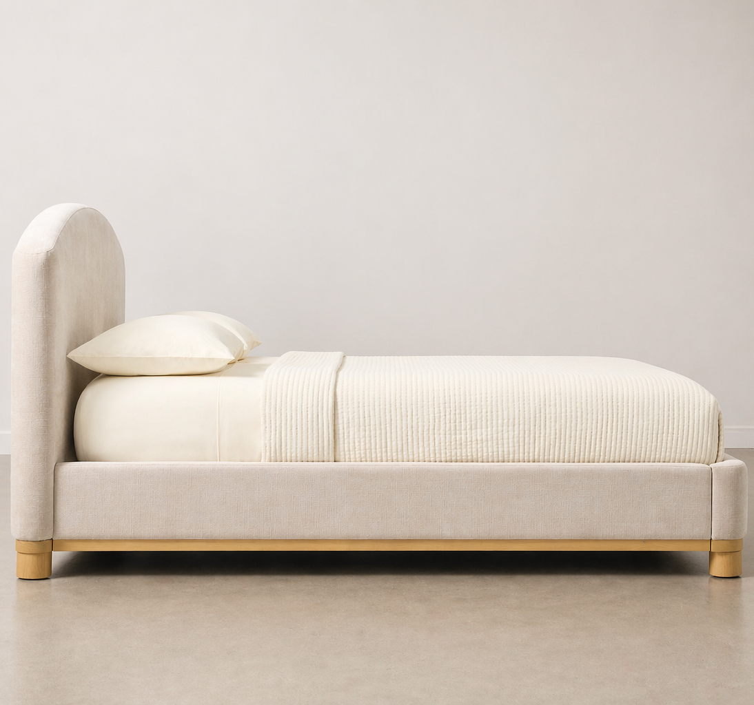 Beige bed with white bedding against a plain wall